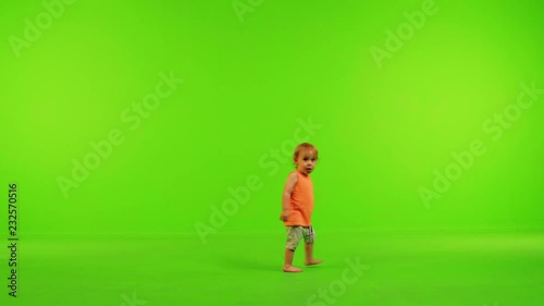 Cute little toddler walks happily from side to side, stops and eat in a full shot over a green screen.
