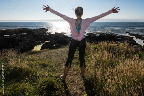 Adult female stands with her arms raised in happiness and freedom while on vacation at Cape Perpetua along the Oregon coastline