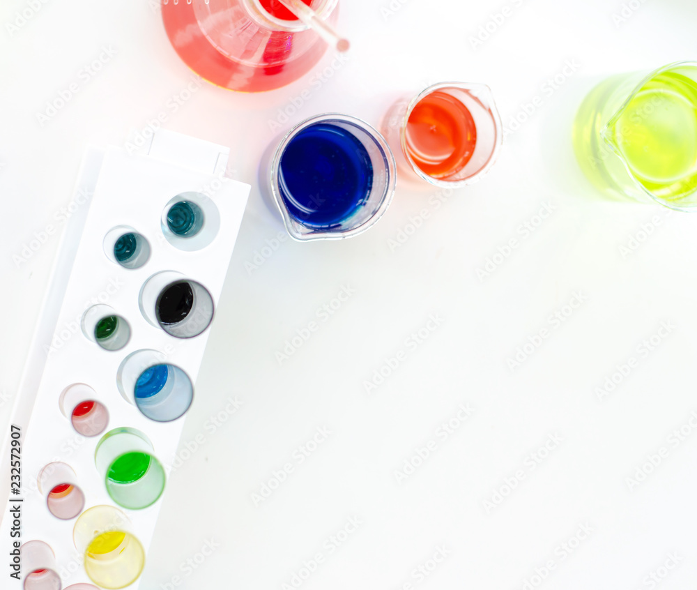 top view of laboratory equipments. A blue liquid watch glass, flask, test tubes and beaker on the white table top view of laboratory equipments. A blue liquid watch glass, flask, test tubes and beaker on the white table