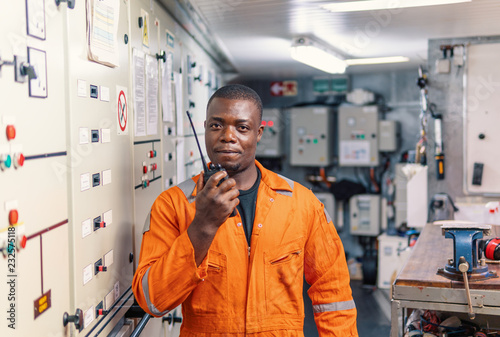 African marine engineer officer in engine control room ECR. He speaks with VHF or UHF portable radio. Ship communication routine photo