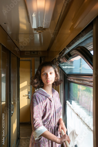 A teenage girl is standing in corridor of compartment car of train, traveling