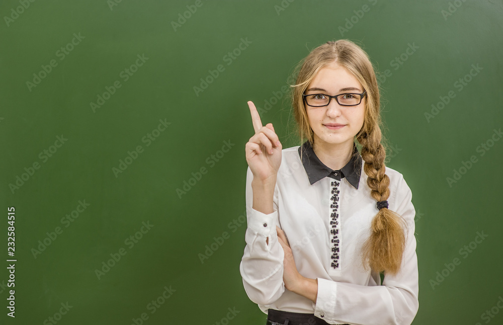 Teen girl standing near green chalkboard and pointing on empty space Teen girl standing near green chalkboard and pointing on empty space