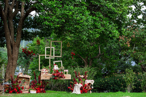 An outdoor wedding, a dessert area under a tree, with cakes and desserts on the dessert table.green gass