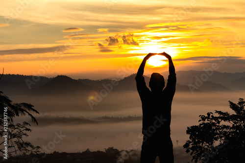 Silhouette of human holding sunlight at morning foggy with sunrise