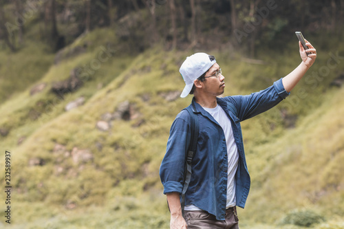 Young Asian traveler man taking photo or selfie outdoors scenic nature background. Lifestyle and relaxation concept. © tuaindeed