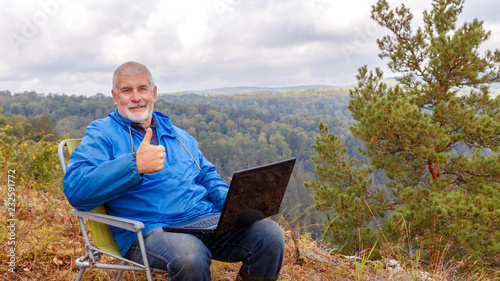 Mature male tourist is working on a laptop on top of the High Mountain. photo