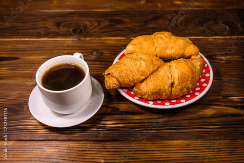 Cup of dark coffee and croissants on wooden table