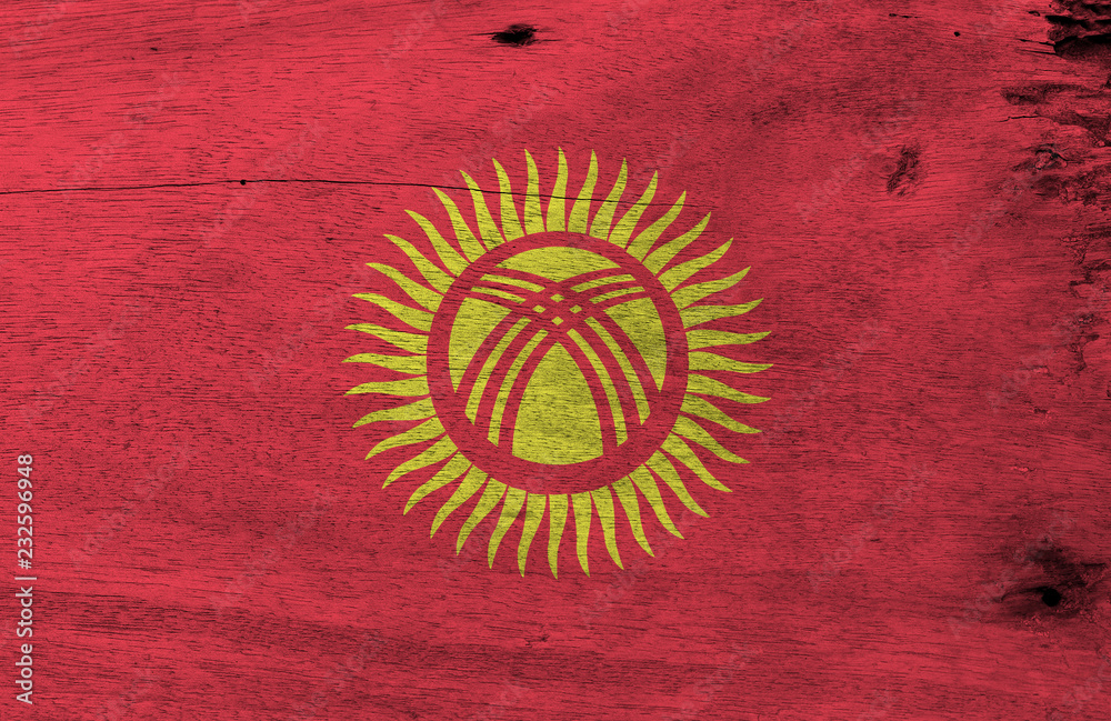 Flag of Kyrgyzstan on wooden plate background. Grunge Kyrgyz flag texture, red field with a yellow sun with forty uniformly spaced rays.