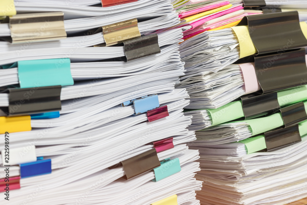 Close up pile of unfinished homework assignment stacked in archive with colorful paper clips on teacher's table waiting to be managed and inspected. Stack of paperwork. Education and business concept. Close up pile of unfinished homework assignment stacked in archive with colorful paper clips on teacher's table waiting to be managed and inspected. Stack of paperwork. Education and business concept.
