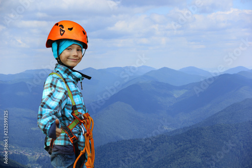 Portrait of a smiling six year old boy wearing helmet and safety harness in mountains, showing like symbol gesture, negative space
