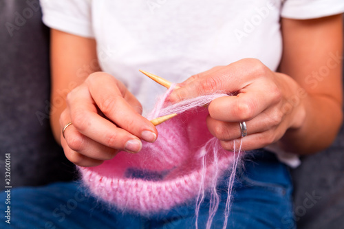 Close-up of an young woman in white t-shirt and jeans, knits a natural wool hat with knitting needles.