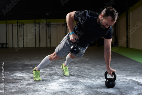 Mature athlete lifting kettle weights for exercising in a gym photo