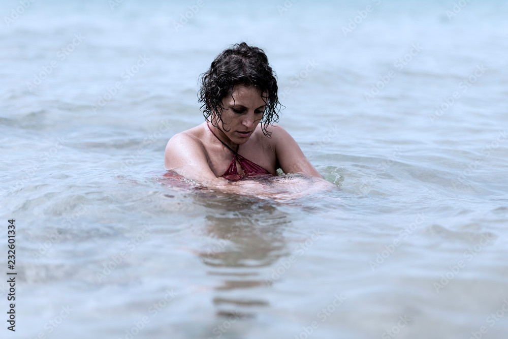 Worried young woman sitting in water wearing a dress