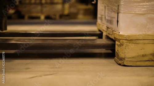 Forklift lifts forks pallets with boxes in warehouse logistics center. Work in warehouse using electric loaders. Close-up of forklift and wooden pallet with boxes during loading.
