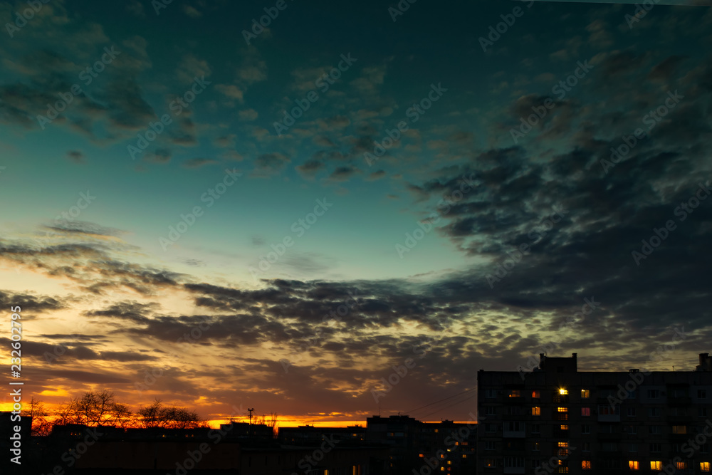 Sky with clouds at sunset over the evening city. Buildings Silhouettes