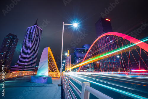 car light trails on steel bridge with city skyline. © hallojulie