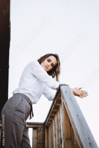 Fashion portrait of a beautiful girl near on the steps of a wooden house by the lake. Posing and resting at sunset. Emotional portrait of a girl © Oleksandr