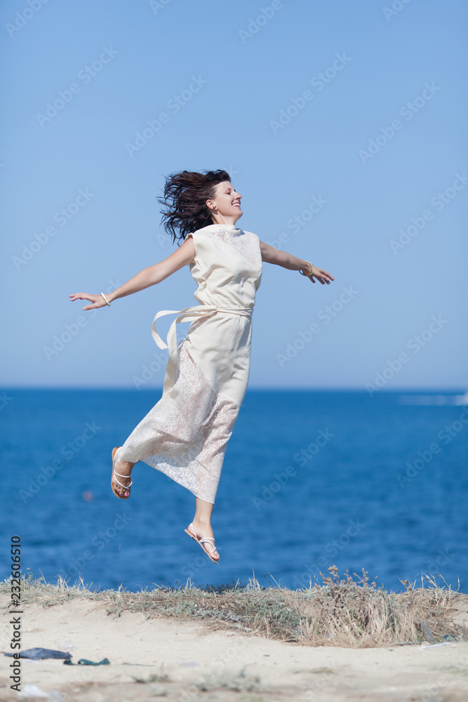 Middle aged woman hopping against sea with arms outstretched Middle aged woman hopping against sea with arms outstretched