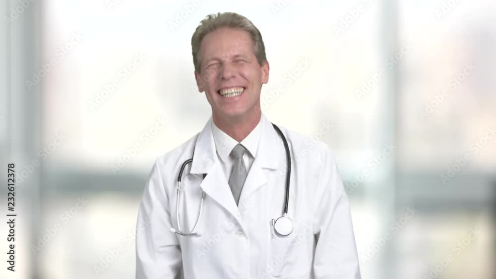 Mature doctor laughing on blurred background. Middle-aged male doctor in white coat is laughing. Joyful middle-aged doctor. Mature doctor laughing on blurred background. Middle-aged male doctor in white coat is laughing. Joyful middle-aged doctor.