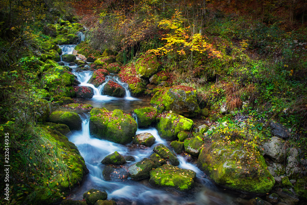 Colorful picturesque autumn landscape of river with small waterfalls and mossy stones