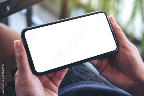 Mockup image of woman's hands holding and using a black mobile phone with blank screen horizontally for watching