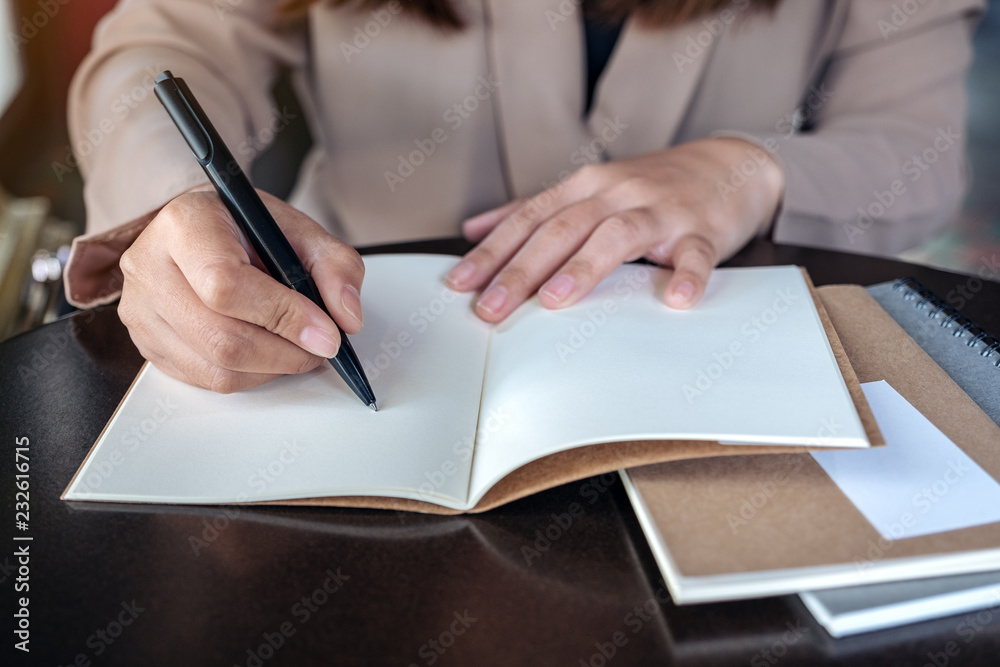 Closeup image of a business woman writing on blank notebook on wooden table Closeup image of a business woman writing on blank notebook on wooden table