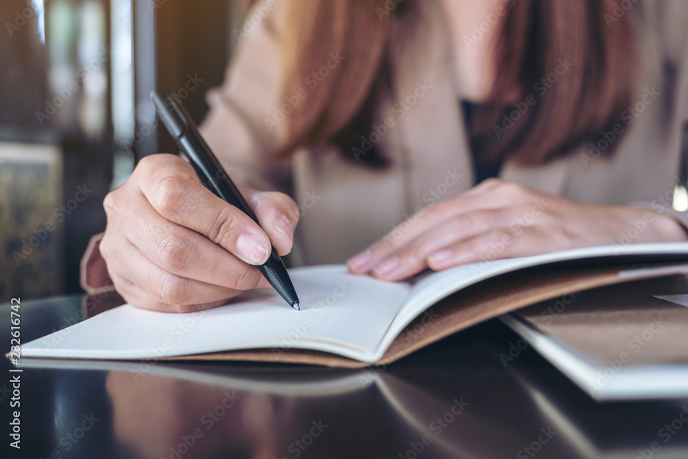 Closeup image of a business woman writing on blank notebook on wooden table Closeup image of a business woman writing on blank notebook on wooden table