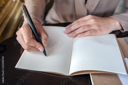 Closeup image of a business woman writing on blank notebook on wooden table
