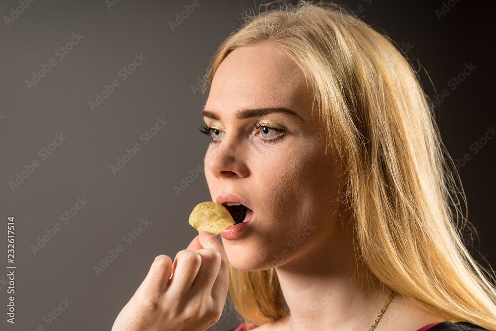 Junk food and unhealthy eating concept. Portrait of young woman who holding fried potato chips at the mouth, posing over gray background. Studio shot Junk food and unhealthy eating concept. Portrait of young woman who holding fried potato chips at the mouth, posing over gray background. Studio shot