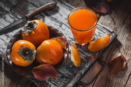 Ripe orange persimmon fruit and persimmon leaves in a brown plate on a brown wooden table photo