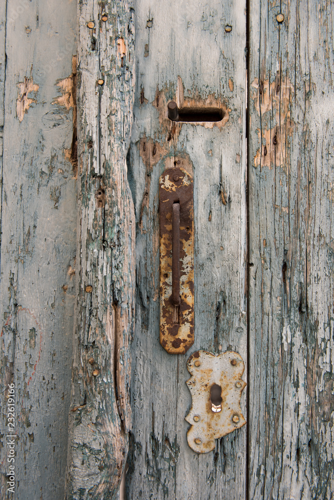 Old and rusty door knob with keyhole on pale and vintage blue wooden doors.
