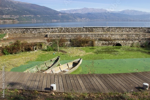 Old tranditional fishing boats in a small dirty harbor with green water in lake Pamvotis in Ioannina Greece view of mountains in the background photo