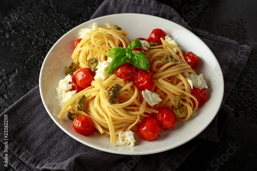 Pasta with green pesto sauce, roasted cherry tomatoes and mozzarella cheese in white plate on dark rustic background