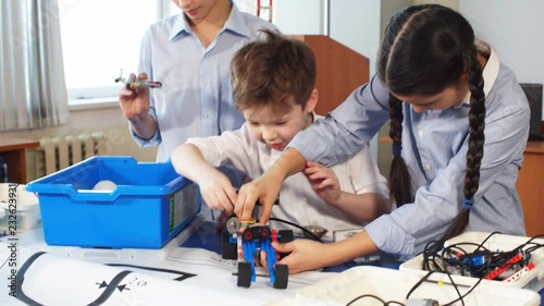 Fair haired cheerful little boy making a robot from metal parts and microcircuits, his brother and sister help him, close up. Happy emotion and enjoyment. photo