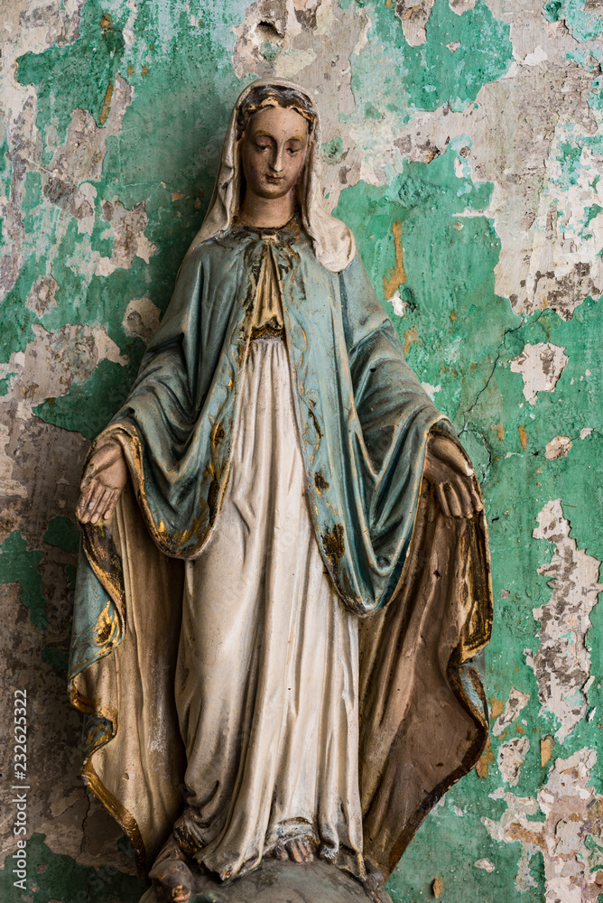 Old Virgin Mary statue, peeling paint grunge wall background of an abandoned building