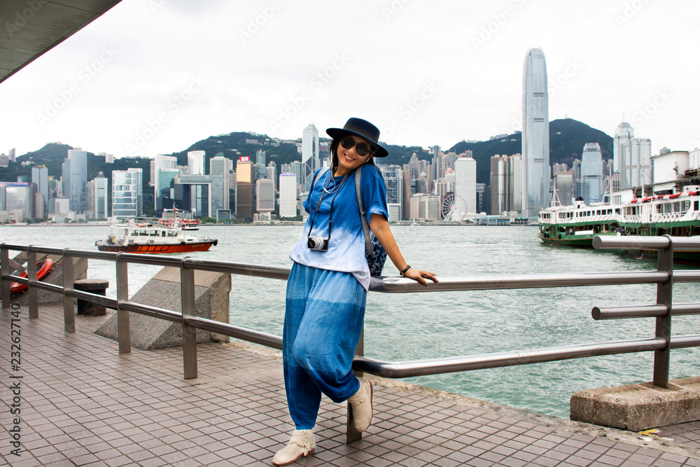Fototapeta premium Podróżujący tajska kobieta pozuje do zrobienia zdjęcia z widokiem na krajobraz i panoramę wyspy Hongkong na molo w porcie Wiktorii