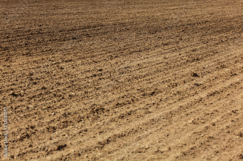 Freshly ploughed field, lines from plow visible in ground. Abstract agriculture background.