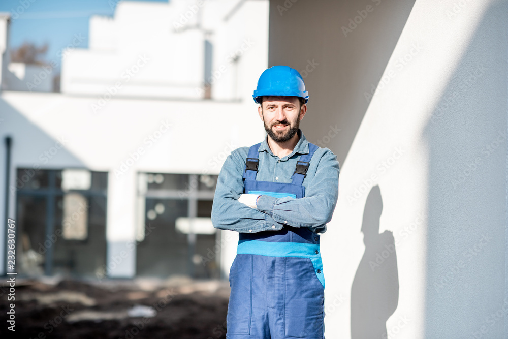 Portrait of a handsome builder in uniform on the construction site with white houses on the background Portrait of a handsome builder in uniform on the construction site with white houses on the background