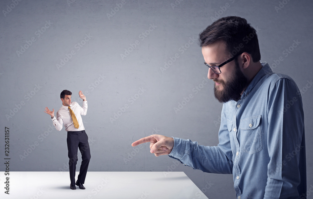 Young professional businessman being angry with an other miniature businessman in front of a grey background Young professional businessman being angry with an other miniature businessman in front of a grey background