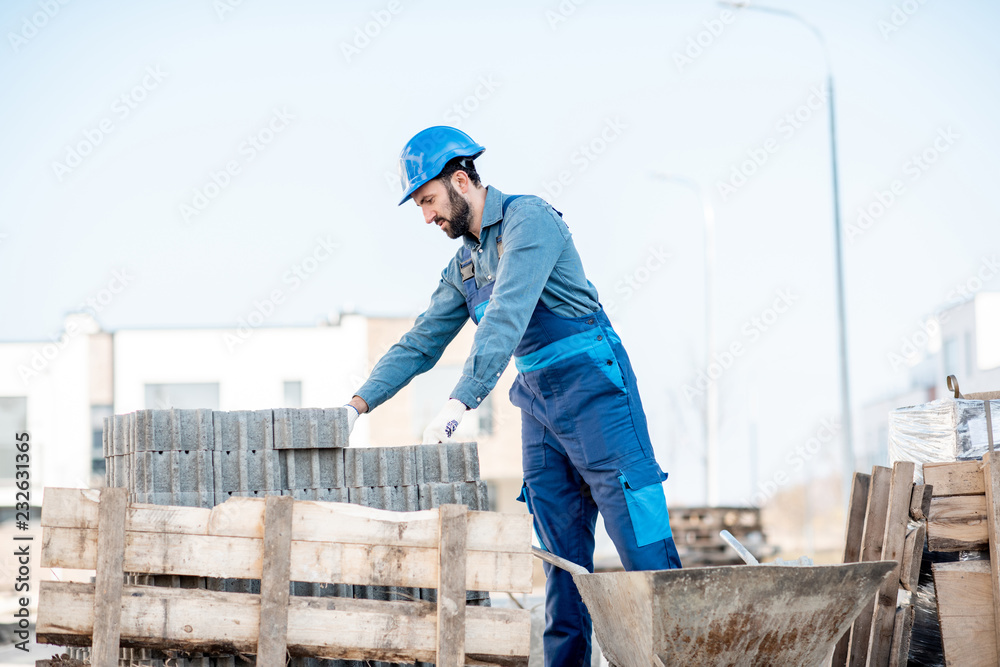 Builder in uniform taking paving blocks from the pallet working on the construction site outdoors Builder in uniform taking paving blocks from the pallet working on the construction site outdoors
