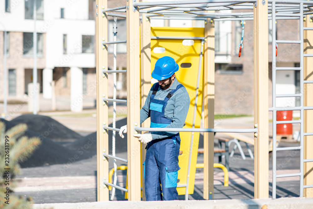 Handsome workman in uniform mounting ladder for kids playing on the playground outdoors