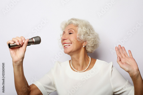 lifestyle and people concept: Portrait of charming modern grandmother holds up the microphone stand and sings