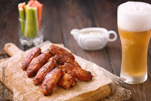 Roasted chicken wings served on a wooden board with glass of beer, carrot, celery and sause