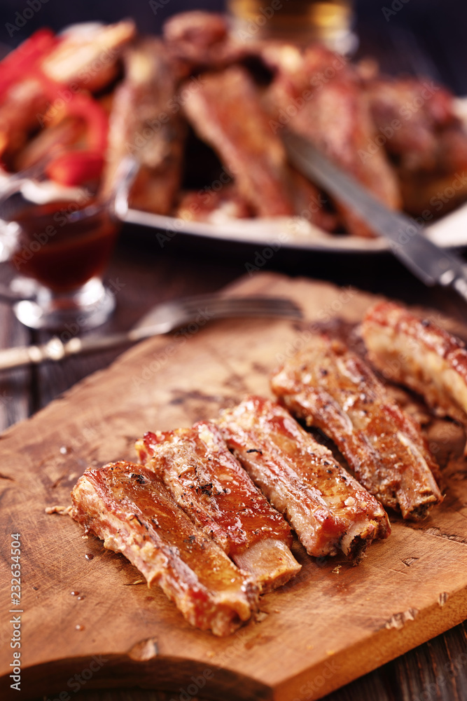 Roasted spare ribs on a wooden board with fork, knife and glass of beer on a rustic wooden table