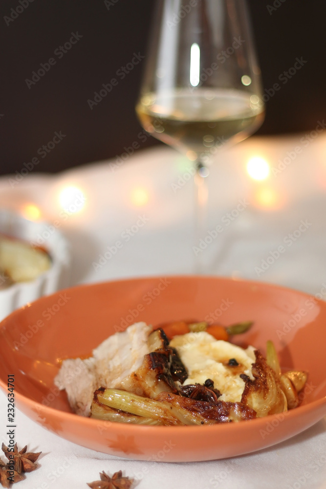 Plate with pork belly roast, mashed potatoes and roasted vegetables. Glass of white wine in the background. Served on a holiday table. Selective focus.