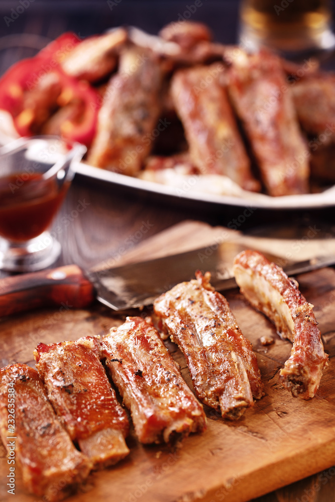 Cooked spare ribs on a wooden board with meat hatchet, BBQ sauce and glass of beer on a rustic wooden table