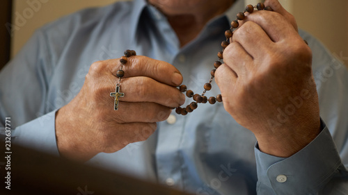 Praying hands of an old man holding rosary beads.