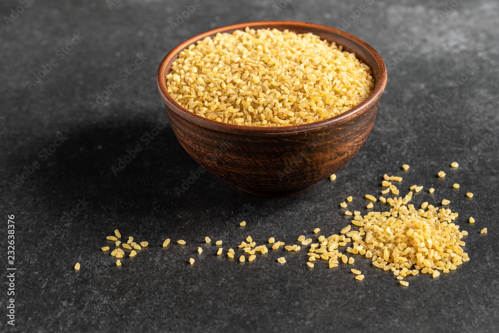 useful bulgur groats in ceramic dishes on a dark, gray, stone background useful bulgur groats in ceramic dishes on a dark, gray, stone background