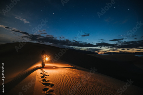 portrait of a woman with lantern walking on sand dunes at night photo