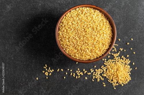 useful bulgur groats in ceramic dishes on a dark, gray, stone background photo